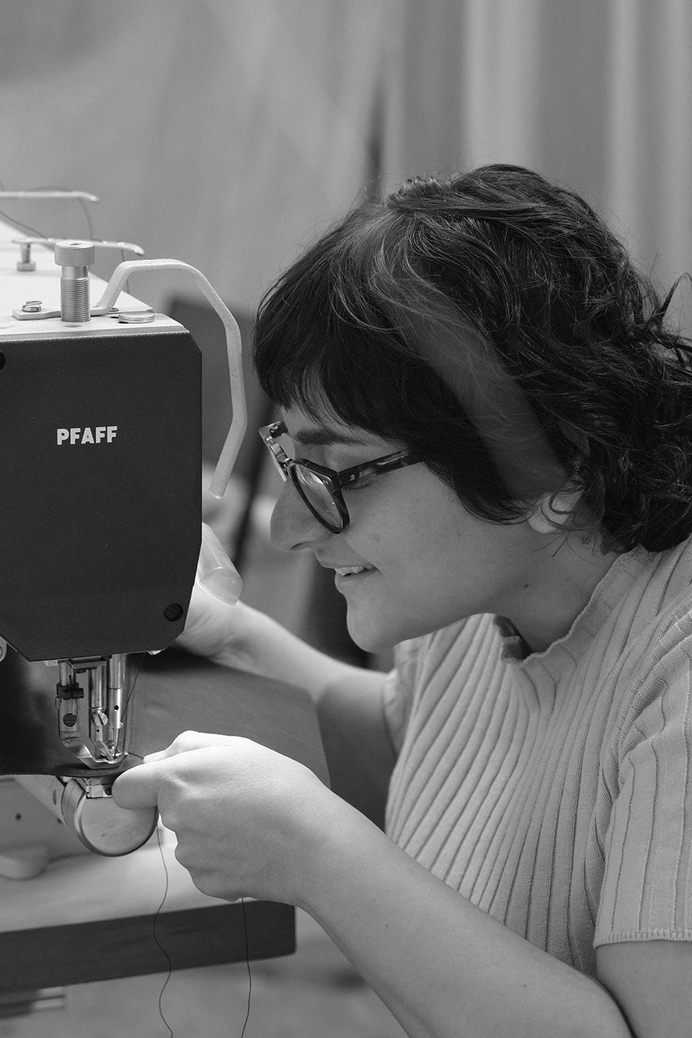 Simone Agius in the simétrie atelier. She is at the sewing machine sewing and smiling.