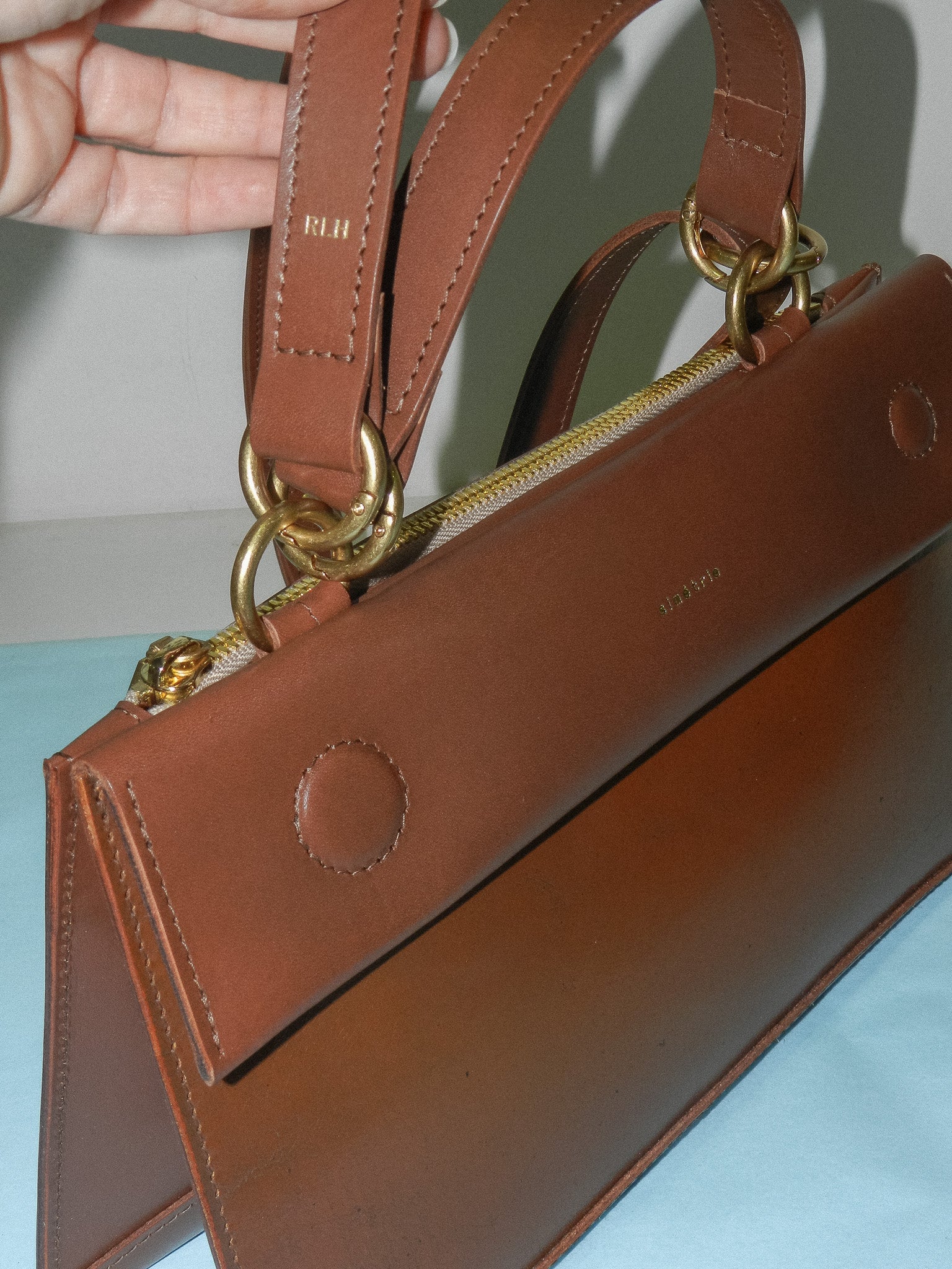 A personalised custom Bay Bag in Red Rock, with sentimental leather from the clients father featured on the front panel. The clients initials are on the strap.