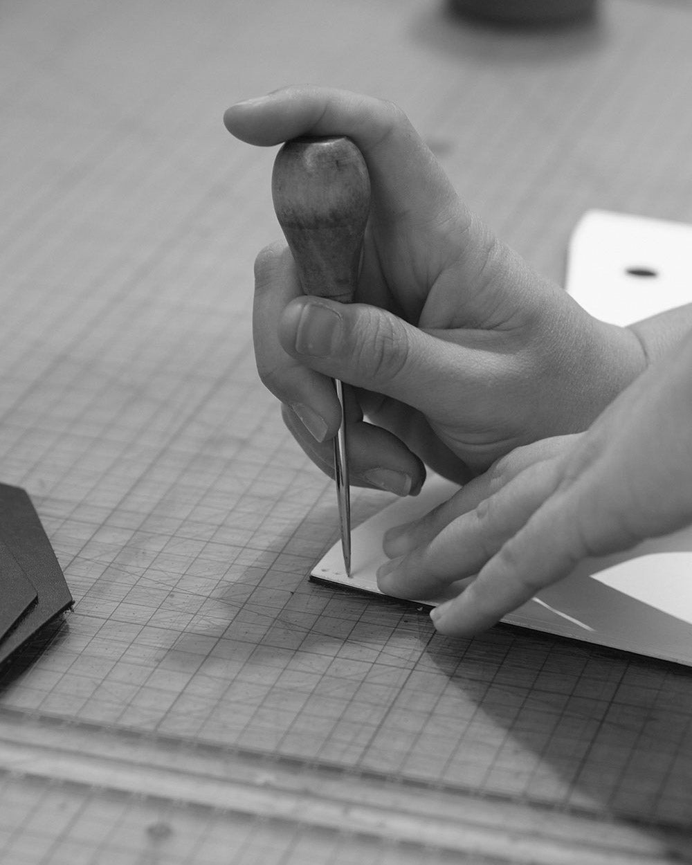 A close up of a hand holding an awl upright, transferring marks through a paper pattern onto a leather panel.