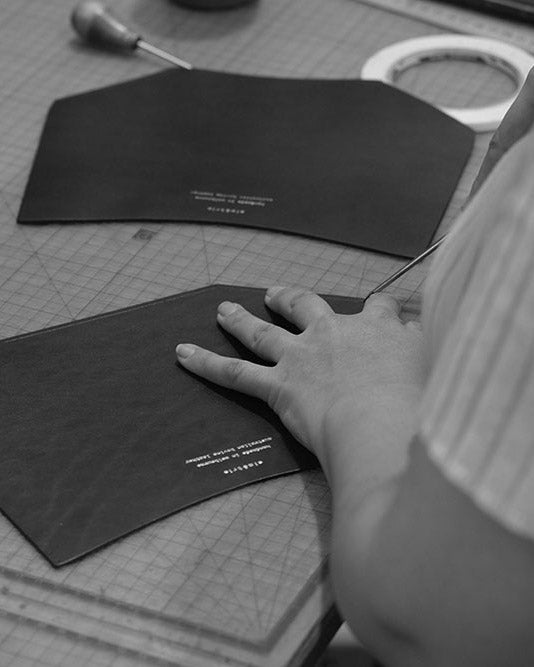 A close up of a workbench with leather bag panels. A woman is working.