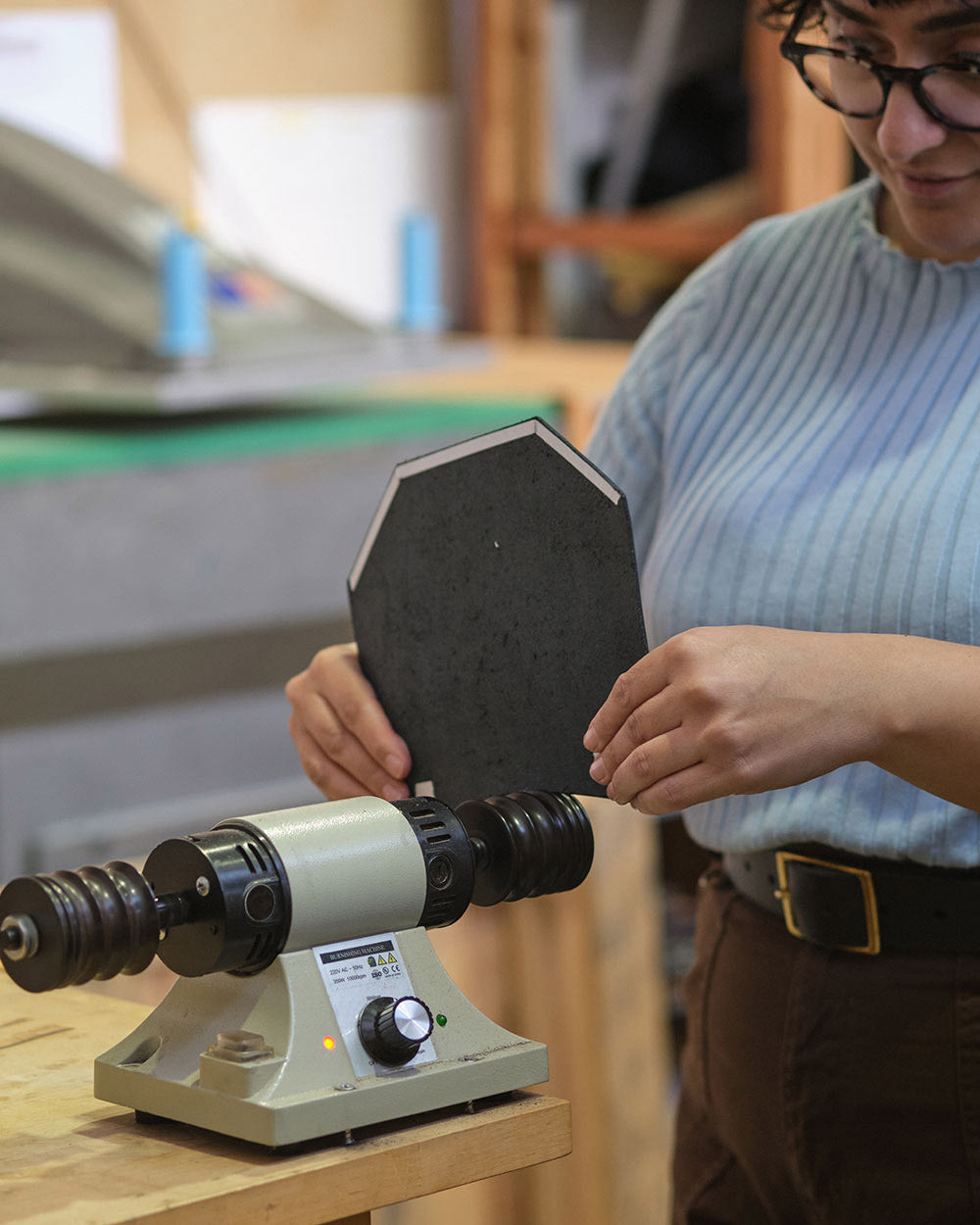 Simone at the burnishing machine. She is looking at the leather bag panel that she has against the machine.