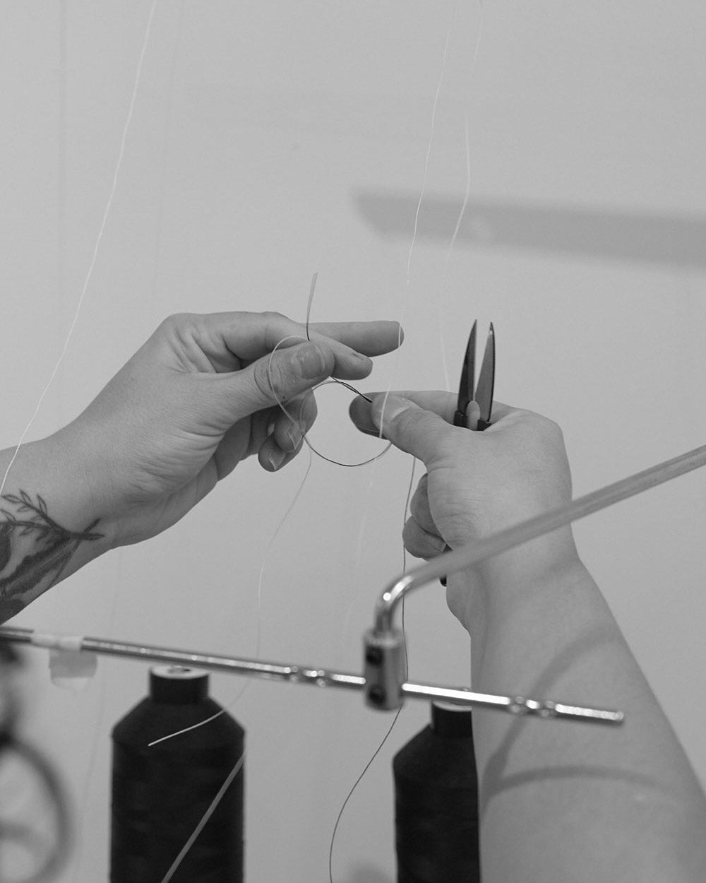 two hands knotting two threads with a pair of snips in one hand.