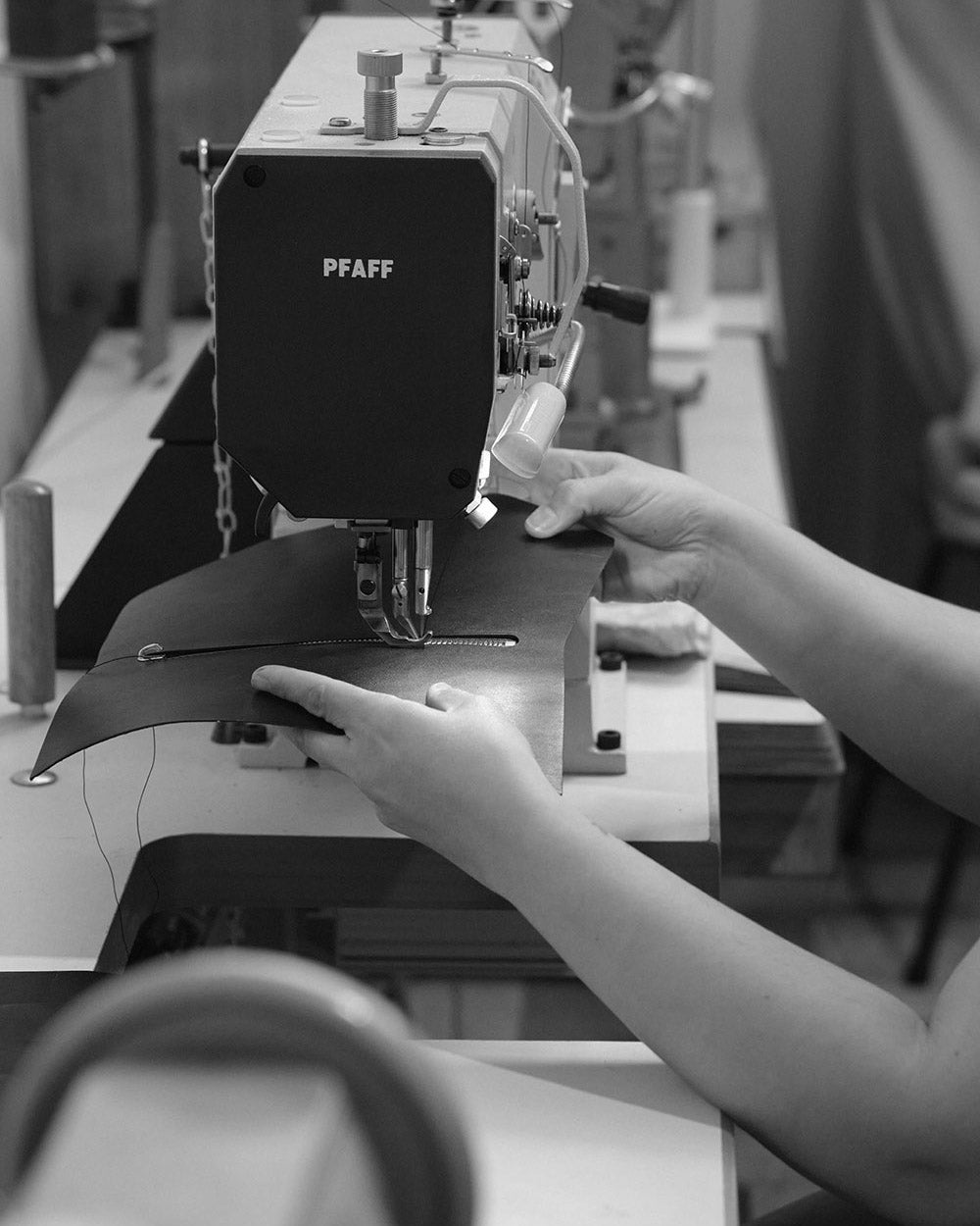 hands guiding a leather bag panel into an industrial sewing machine.