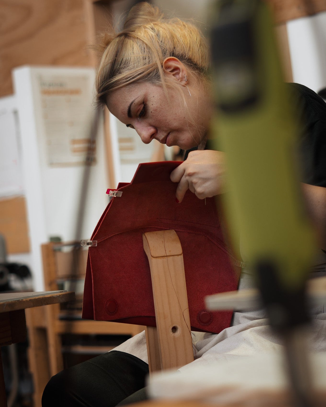 A student saddle-stitching a red bag using a stitching pony.